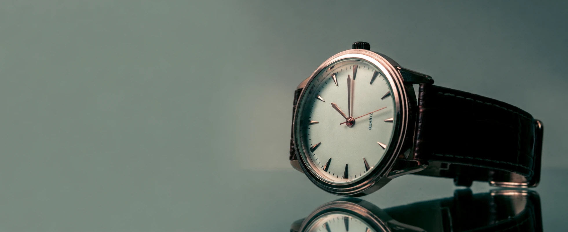 Cream-dial wristwatch with a dark leather strap reflected on a muted green surface